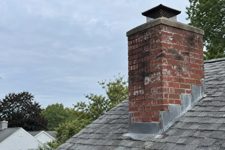 Red brick chimney with a concrete crown, metal cap, and step flashing on an asphalt shingle roof