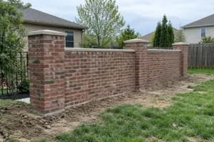 Newly built red brick garden wall with brick columns and light stone caps in a backyard