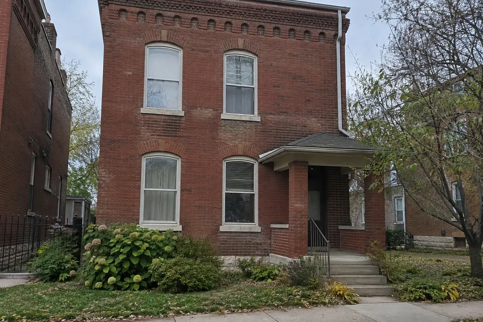 Older two-story red brick house with arched windows and decorative brickwork near the roofline