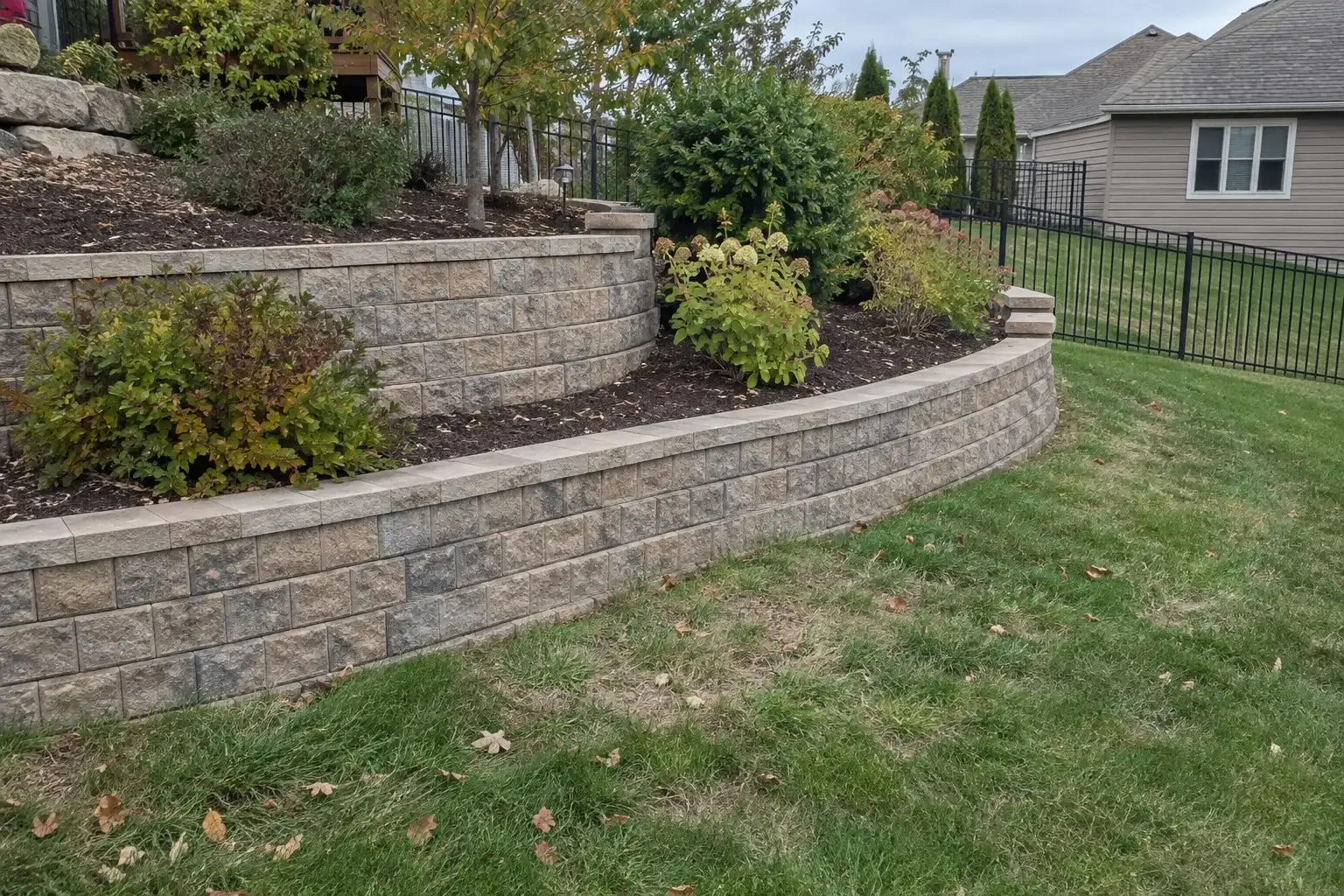 Two-tier segmental block retaining wall terracing a sloped backyard with planting beds